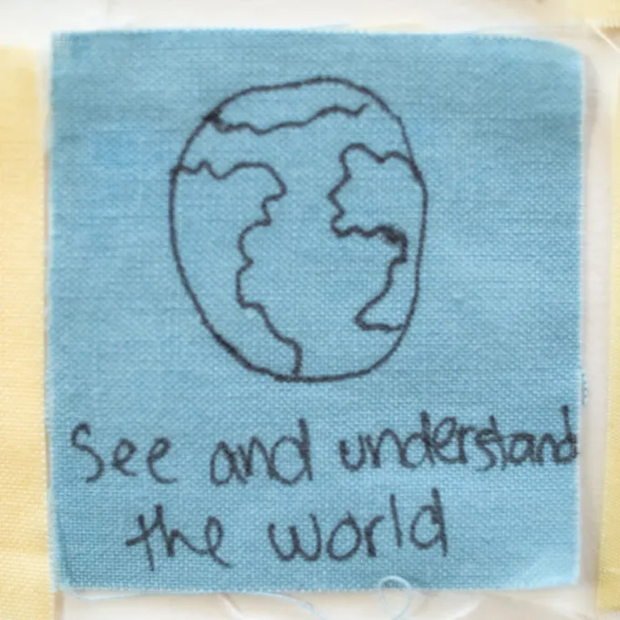 Close up of a senior quilt square that reads, "see and understand the world."